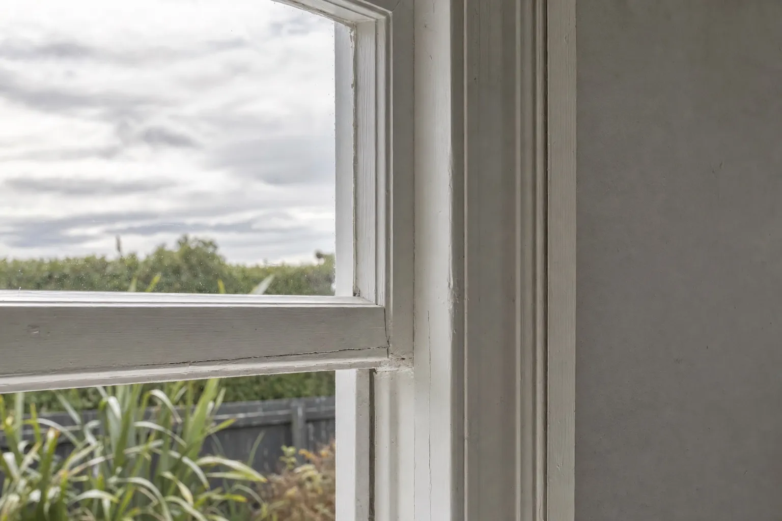 Illustrative photo: a painted timber sash window meeting a moulded architrave in an older room, paint worn at the edges.