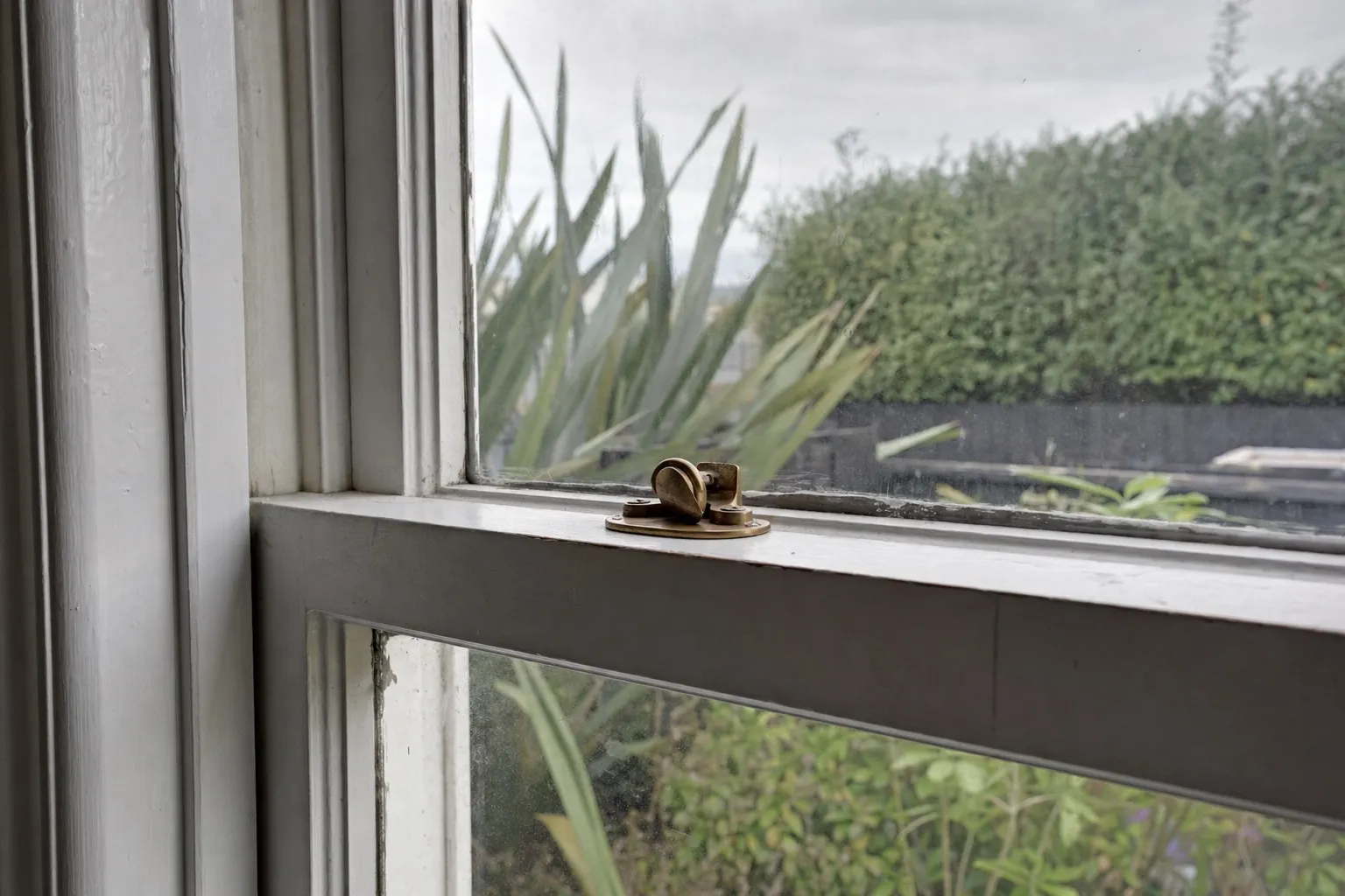Illustrative photo: the meeting rail of a painted timber sash window, with an old brass catch and worn paint.