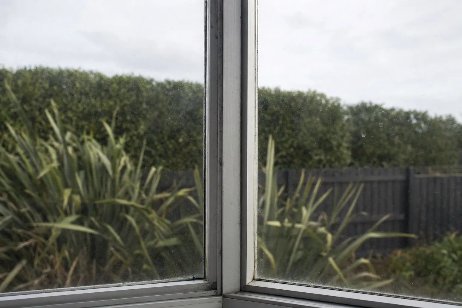 Illustrative photo: the slim frame of an older aluminium window between two panes of glass.
