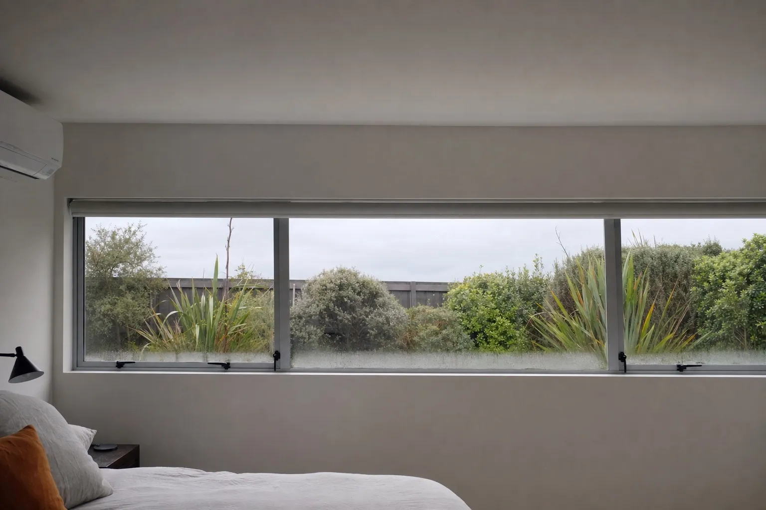 Illustrative photo: a bedroom window on a cold grey morning with a light fog of condensation along the bottom of the glass.