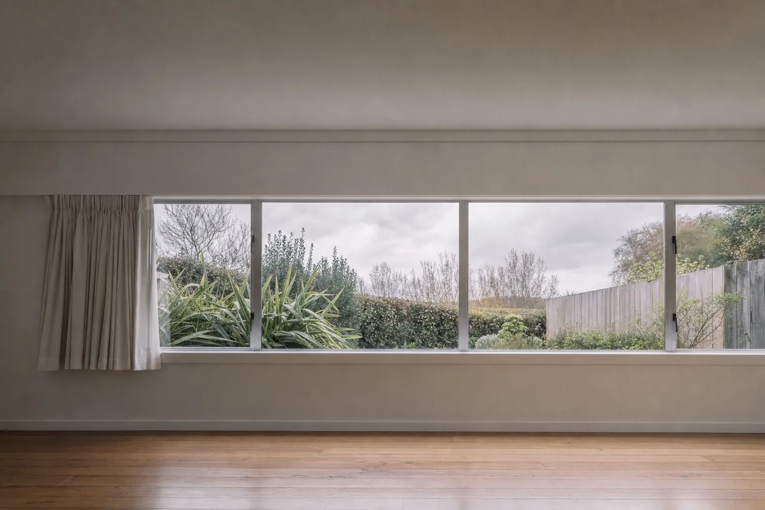Illustrative photo: a plain room with a still curtain beside a wide window and a grey sky outside.